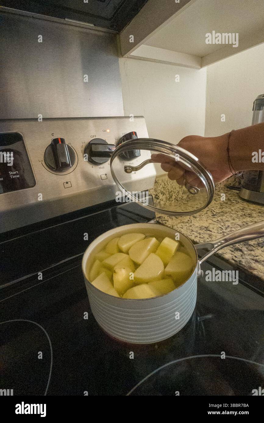 Eine Person kocht Kartoffeln in einem Topf auf einem Herd. Der Topf ist mit einem Deckel bedeckt Stockfoto