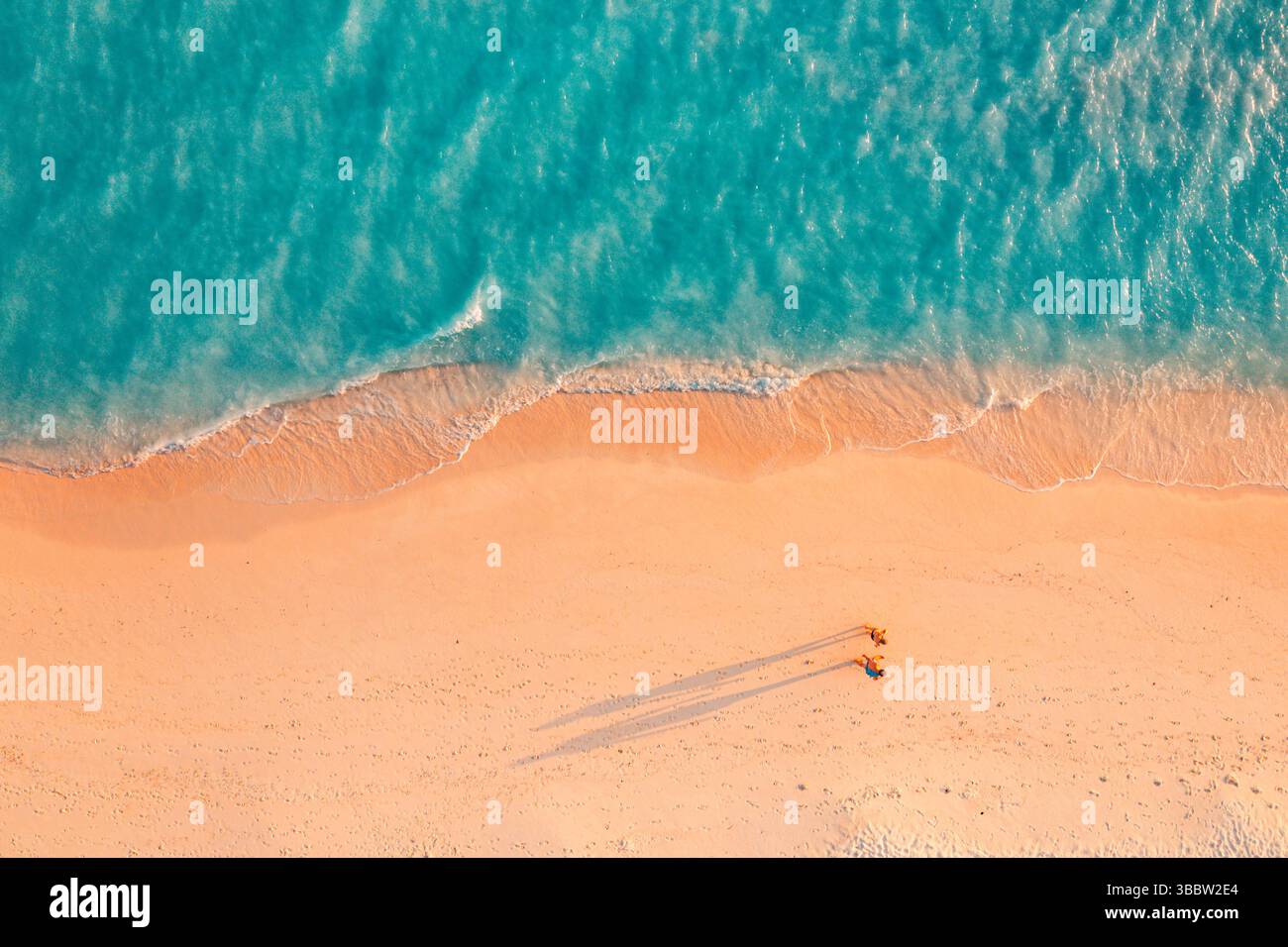 Panoramablick aus der Vogelperspektive tropische Strandwellen Sandpaare Wandern lange Schatten Sonnenschein ruhige Natur atemberaubende Sommerurlaub Insel Landschaft Tapete Stockfoto