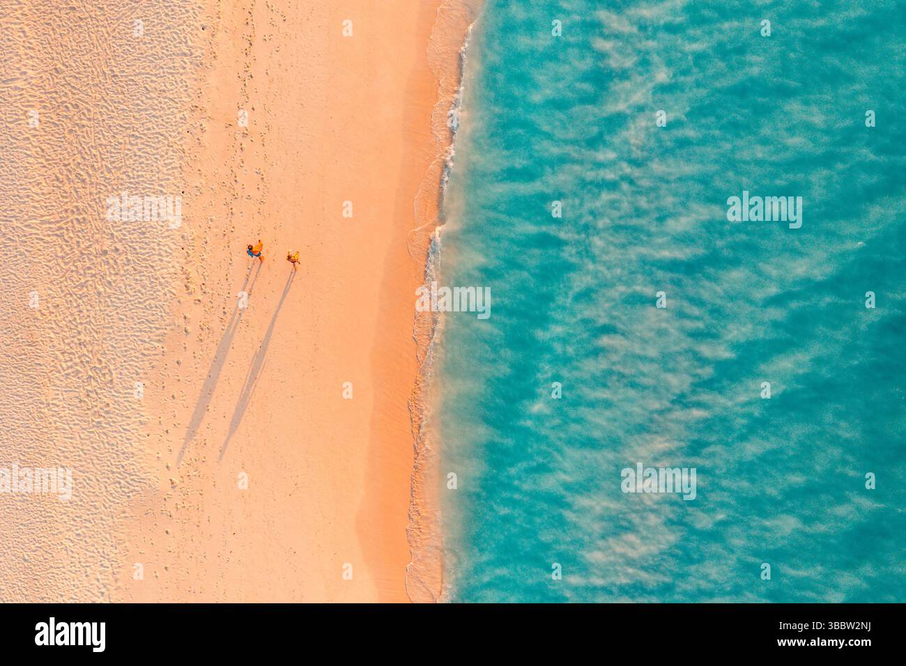 Panoramablick aus der Vogelperspektive tropische Strandwellen Sandpaare Wandern lange Schatten Sonnenschein ruhige Natur atemberaubende Sommerurlaub Insel Landschaft Tapete Stockfoto
