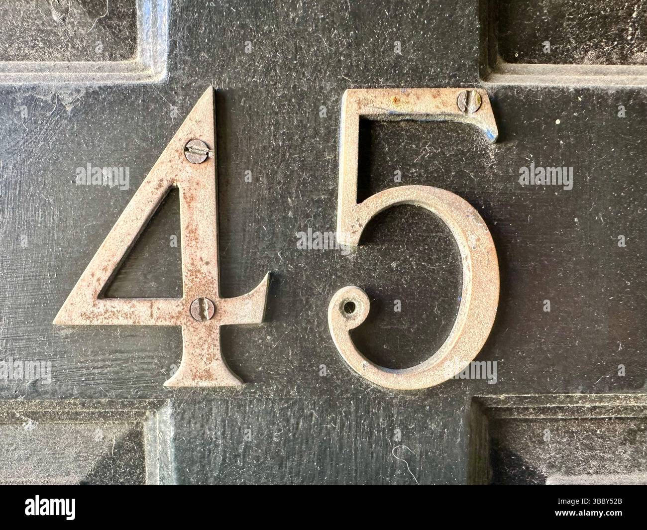Nahaufnahme der staubigen schwarzen Vordertür mit der Metallnummer 45, die Staubpartikel und Spinnennetze auf der Oberfläche zeigt. - Smartphone-aufgenommenes Stockfoto