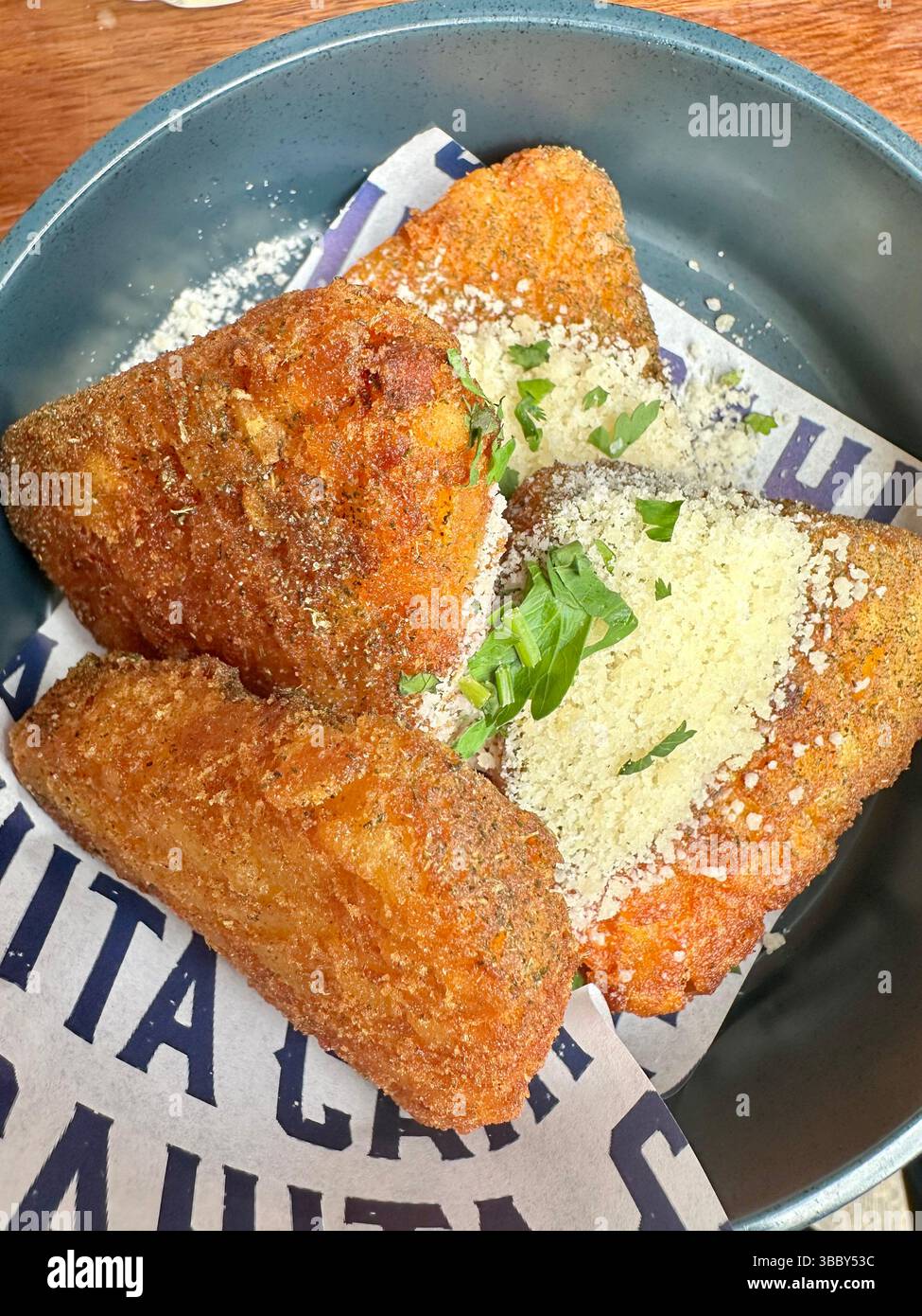 Nahaufnahme von vier in einer grauen Schüssel gestapelten Kartoffelröstchen, garniert mit geriebenem Parmesankäse und gehacktem Schnittlauch. Köstliche Beilage zum Frühstück. - Smartphone-aufgenommenes Stockfoto