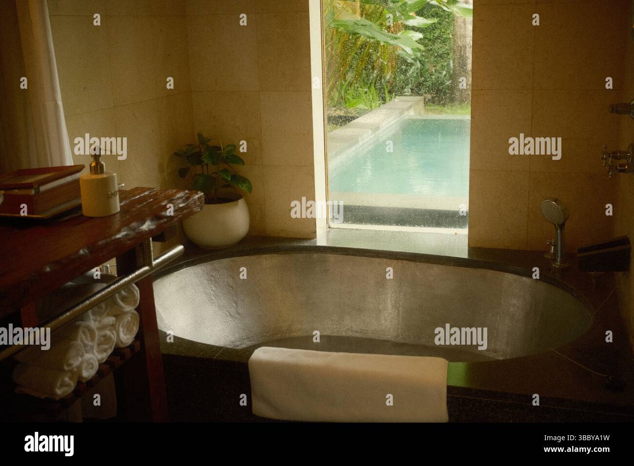 Ruhiges Badezimmer mit Kupferbadewanne und Blick auf den Pool durch ein großes Fenster Stockfoto