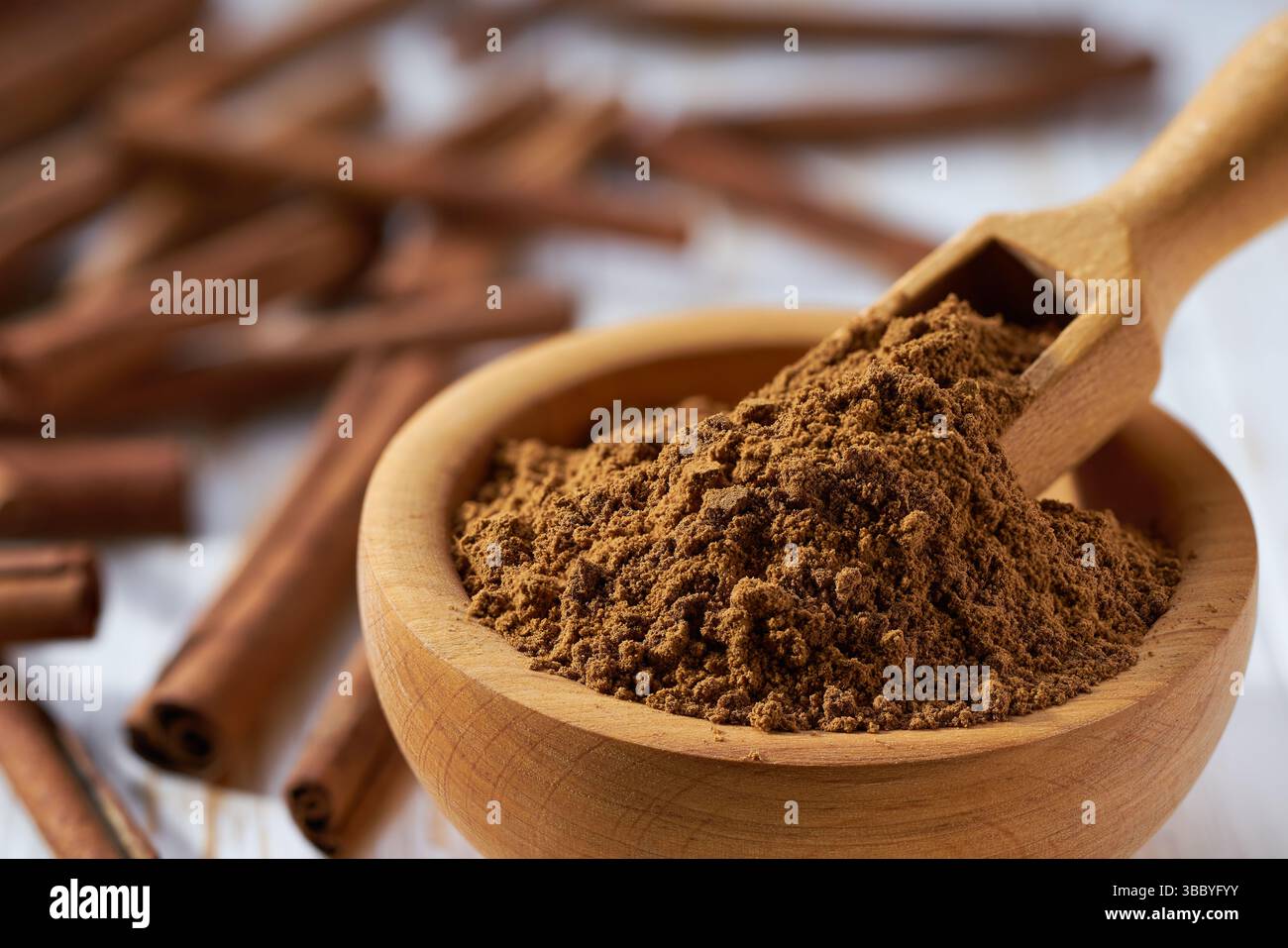 Zimtpulver in einer Holzschale auf einem weißen Holztisch. Stockfoto