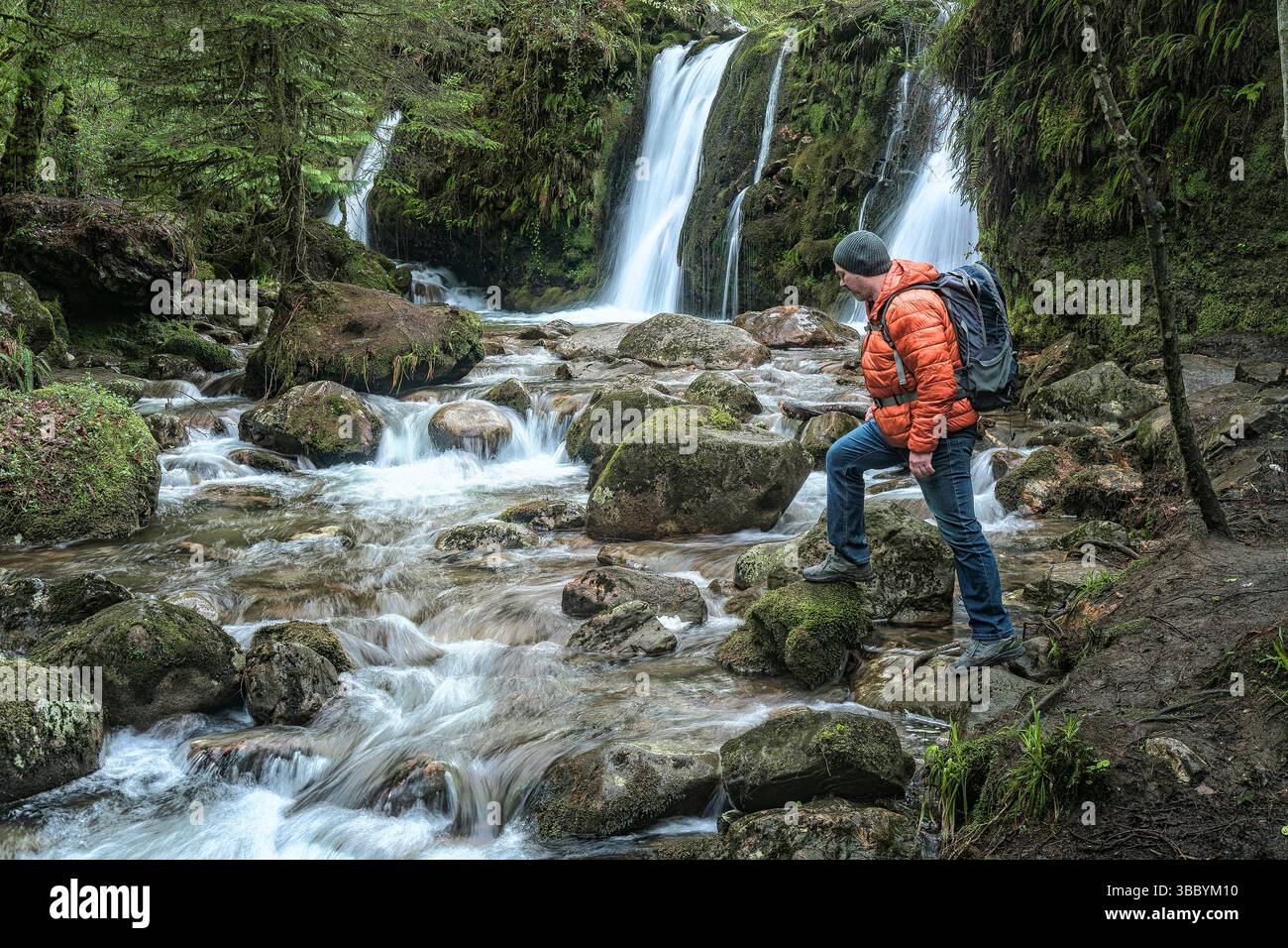 Der Mensch begrüßt die wilde Schönheit von Glenmalure mit Blick auf den Wasserfall und Fluss tief in der irischen Wildnis. Stockfoto