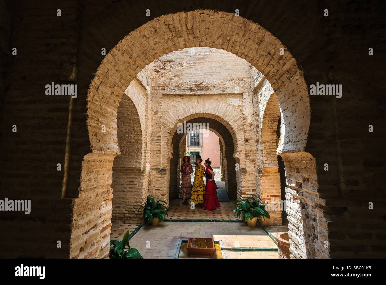 Drei Frauen in traditioneller spanischer Kleidung stehen unter einem Bogen im Alcázar von Jerez de la Frontera, Andalucía, Spanien Stockfoto