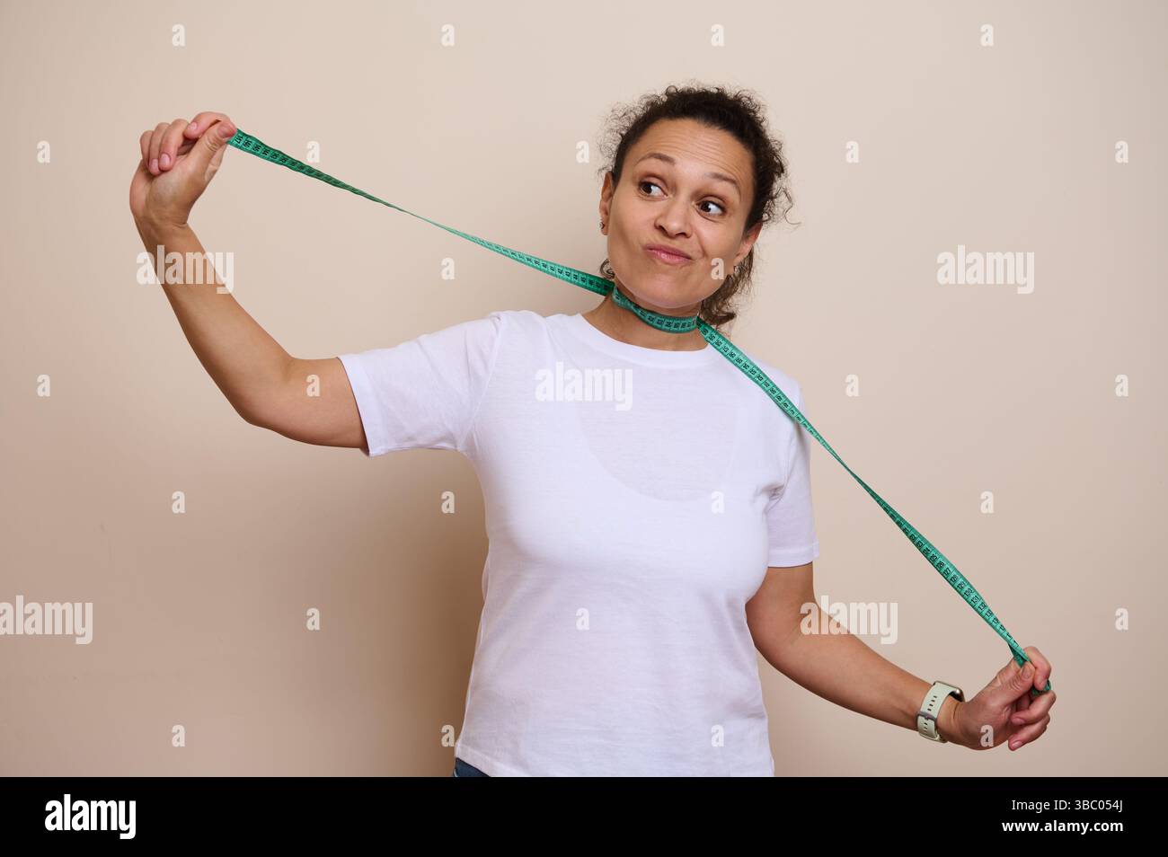 Eine Frau hält ein grünes Maßband, während sie einen durchdachten Blick ausdrückt, der persönliche Gesundheitsentscheidungen, Messziele und ausgewogenes Leben symbolisiert Stockfoto