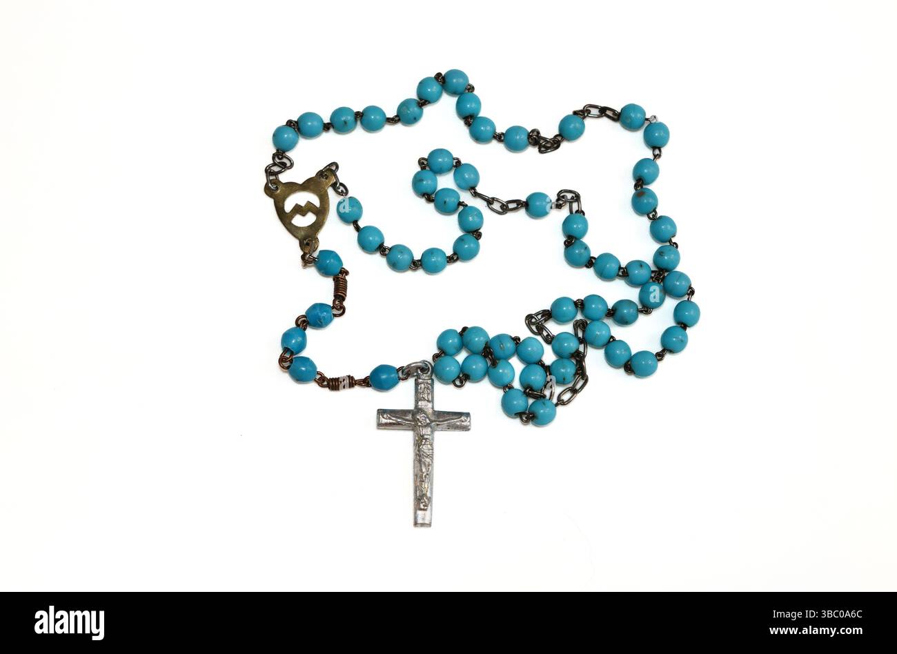 Ein türkisfarbener Rosenkranz mit Perlen und Metallkreuz liegt auf weißem Hintergrund. Der Rosenkranz ist in einem lockeren, unregelmäßigen Muster angeordnet. Die Perlen Stockfoto