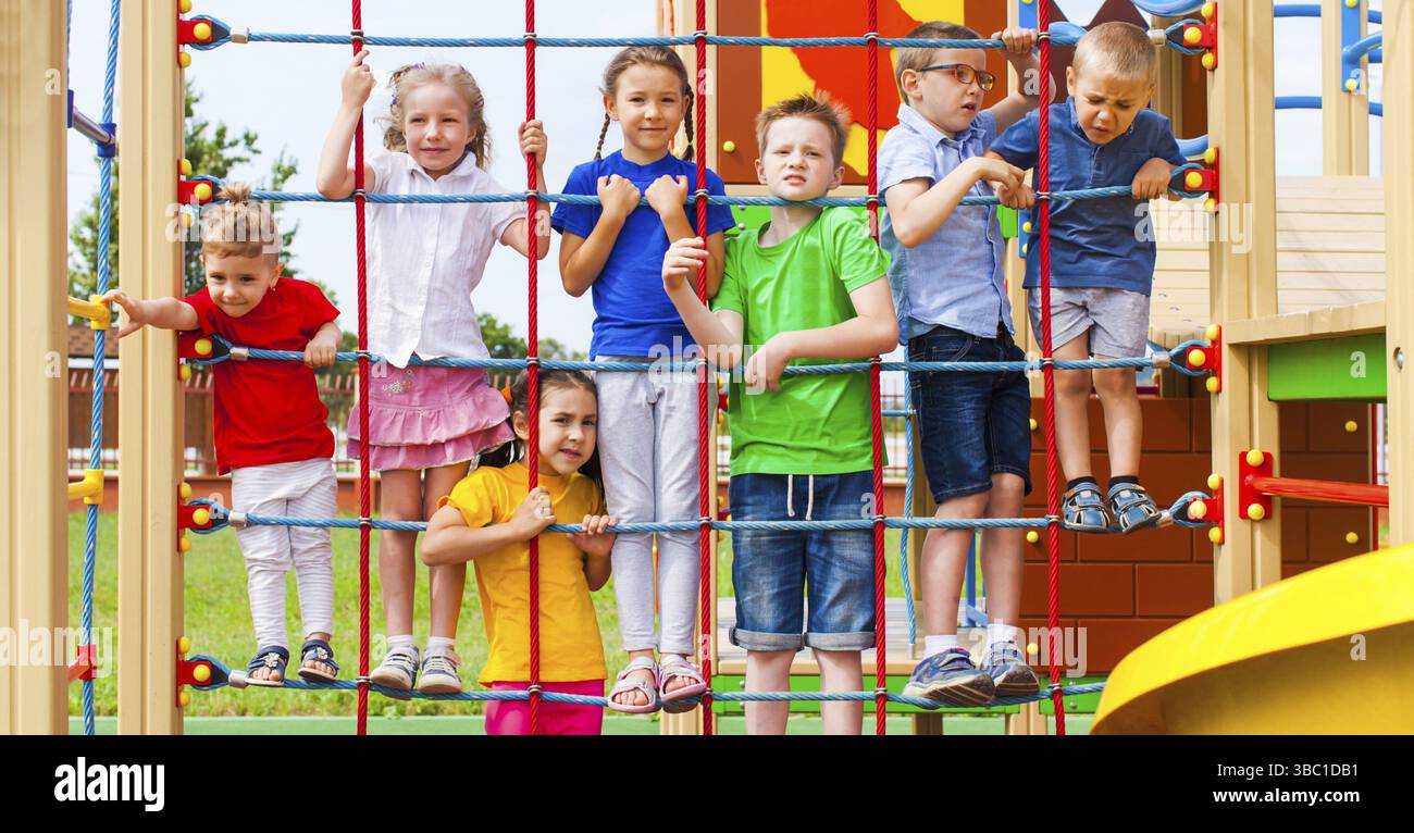 Verspielte Zeit für eine Gruppe bezaubernder Kinder. Farbenfroher Spielplatz im Freien mit Seilnetz und Leiter, viel Ausrüstung für aktive Freizeit Stockfoto