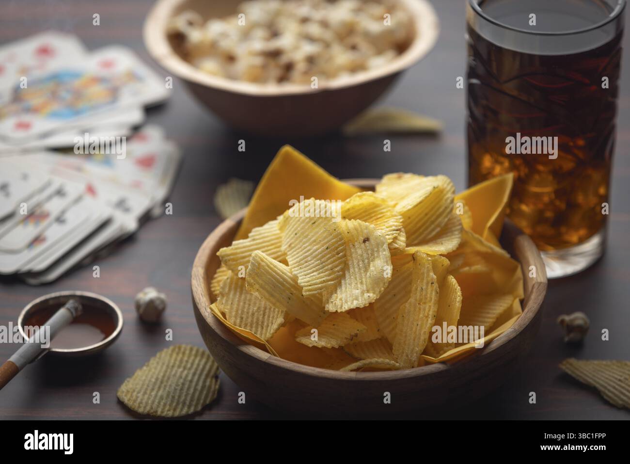 Chips, Popcorn und ein Getränk neben Spielkarten und einer Zigarette Stockfoto