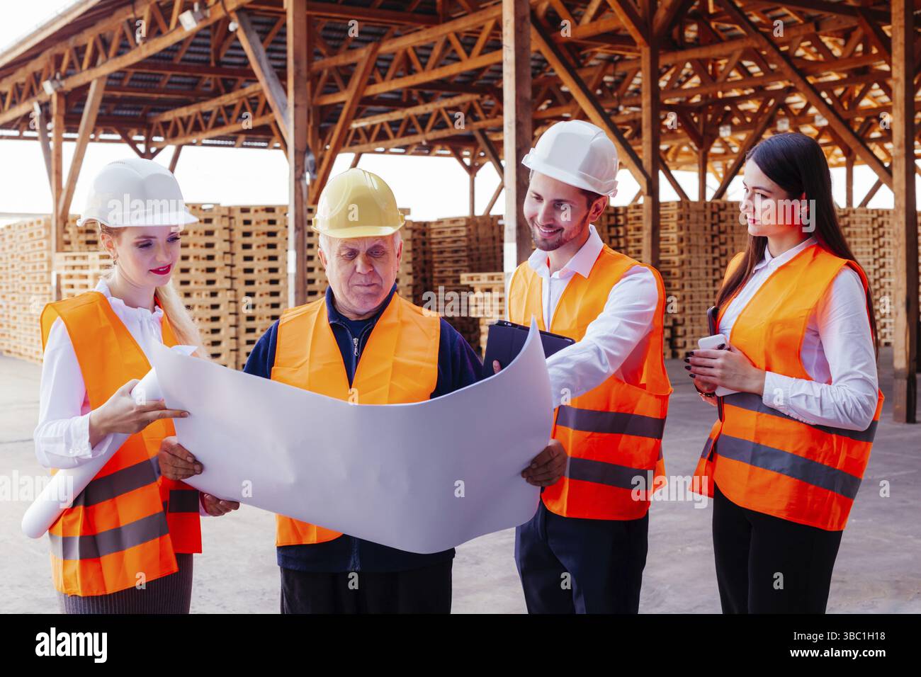 Gruppe von Ingenieuren in Schutzkleidung und Schutzhelmen zur Untersuchung des Papierprojekts der Rekonstruktion. Leitender Fachmann, der sein Wissen und seine Erfahrung weitergibt Stockfoto
