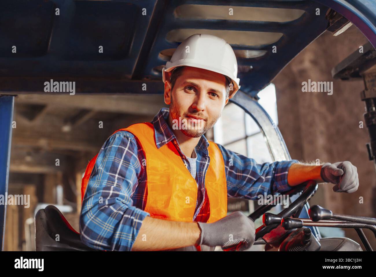Porträt eines jungen, hübschen Lagerarbeiters, der in einem Froklift-Truck sitzt und die Kamera anschaut. Selbstbewusster Gabelstaplerfahrer bei der Arbeit, mit Hardhut und Stockfoto