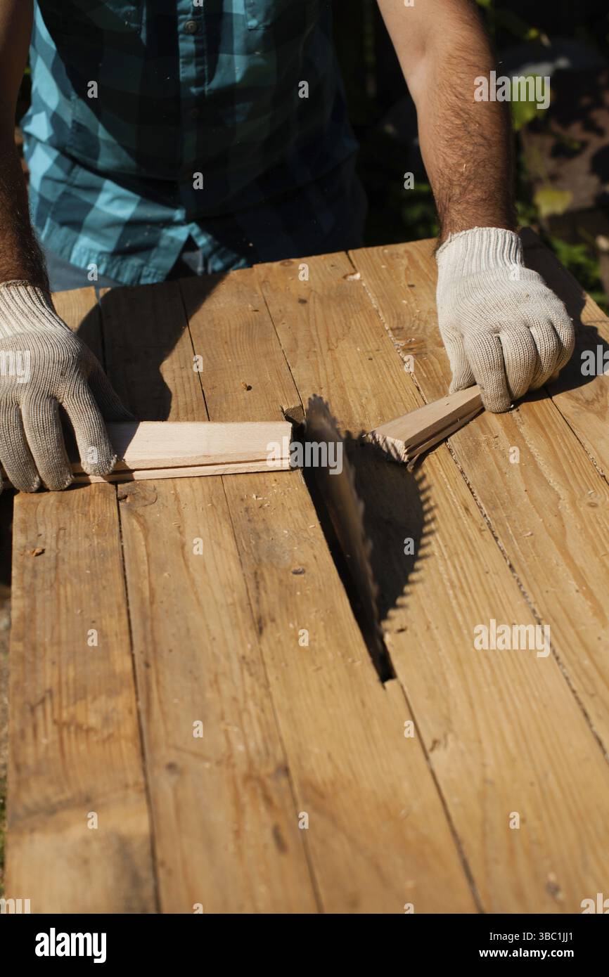 Hart arbeitender Holzarbeiter, der Holzbohlen schneidet, Fokus auf Säge Stockfoto