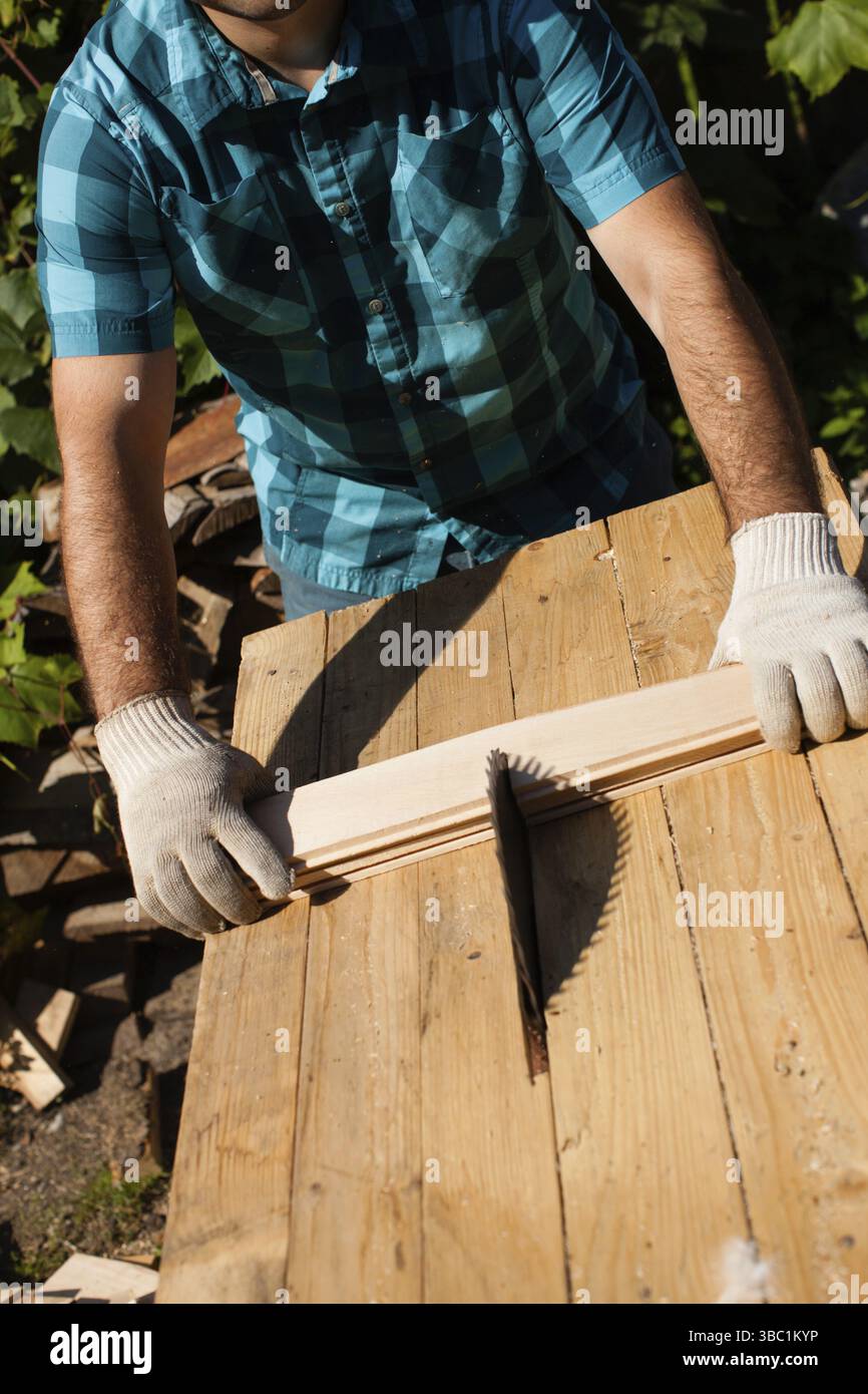 Hart arbeitender Holzarbeiter, der Holzbohlen schneidet, Fokus auf Säge Stockfoto