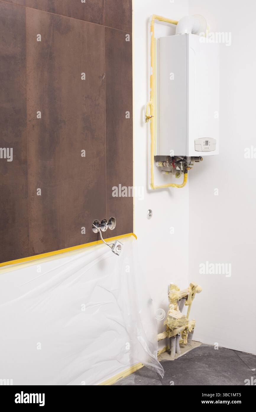 An der Wand befindet sich ein moderner Gaskessel. Der Kessel befindet sich in einem leeren Raum, in dem Reparaturen durchgeführt werden Stockfoto