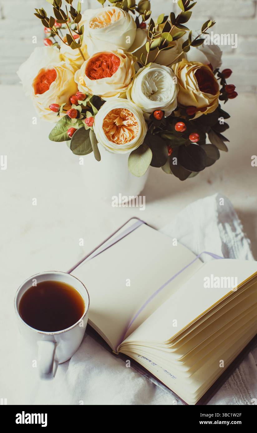 Eine Tasse schwarzen Tee, Notebook und schöne Blumen auf dem Tisch. Morgen-Inspiration für die Tagesplanung Stockfoto