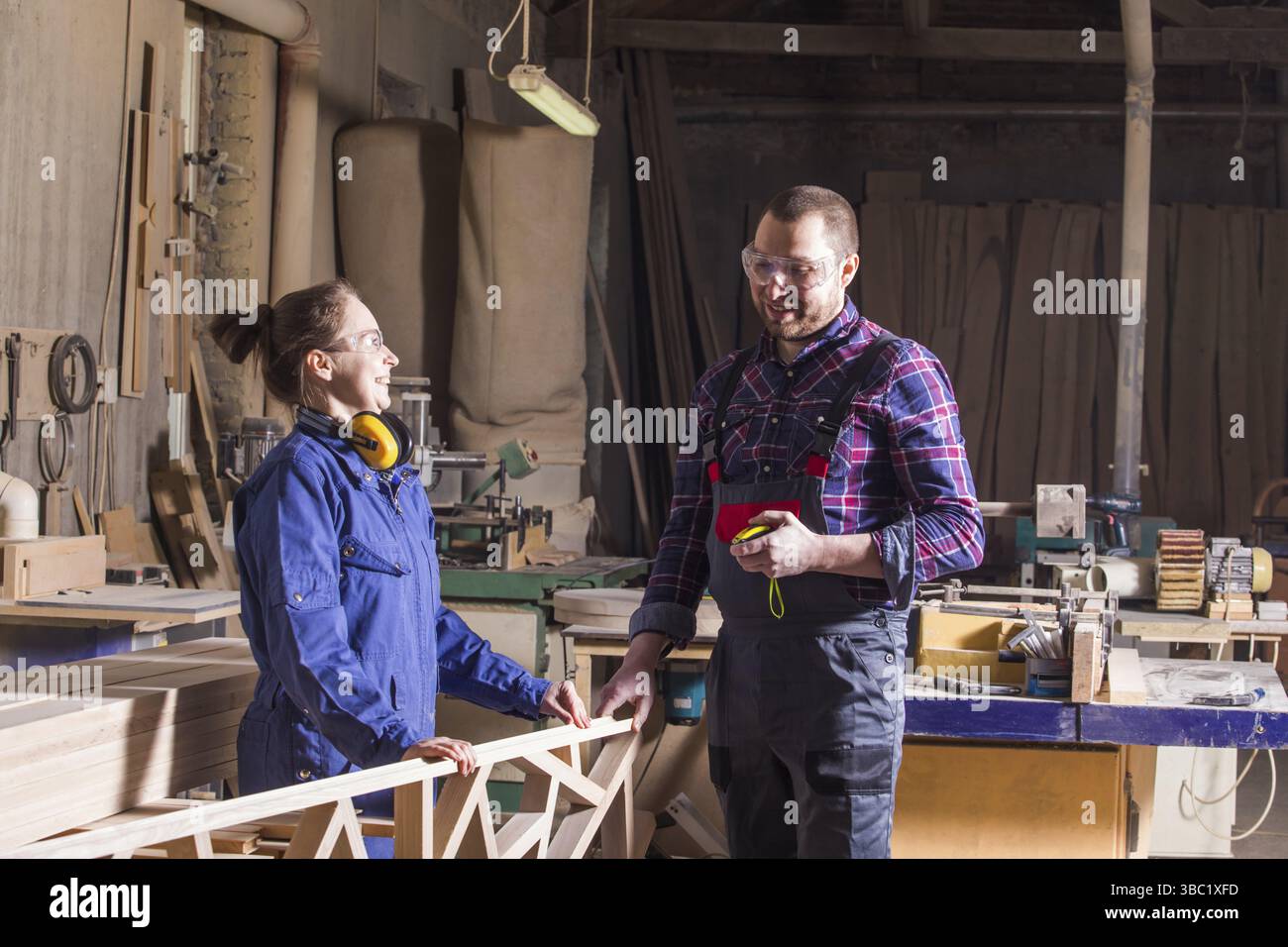 Porträt von Mann und Frau, Zimmerleute in Arbeitskleidung, Herstellung von Holzdekor für das Bett. Kreatives Team von Ehemann und Ehefrau, die in der Möbelarbeit zusammenarbeiten Stockfoto