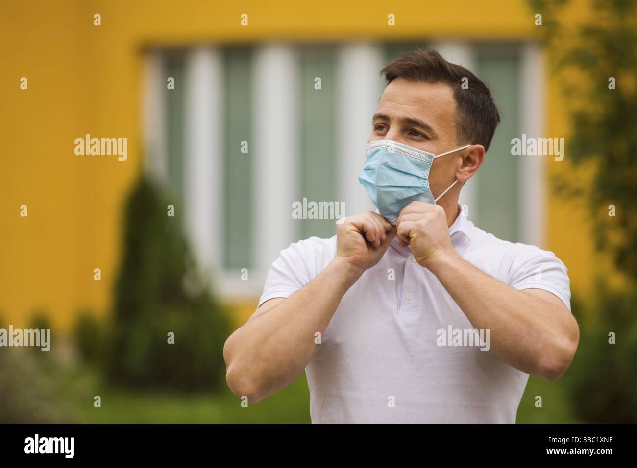 Der gutaussehende junge Mann, der in der Stadt eine medizinische Maske verkleidet. Er trägt ein stilvolles weißes T-Shirt Stockfoto