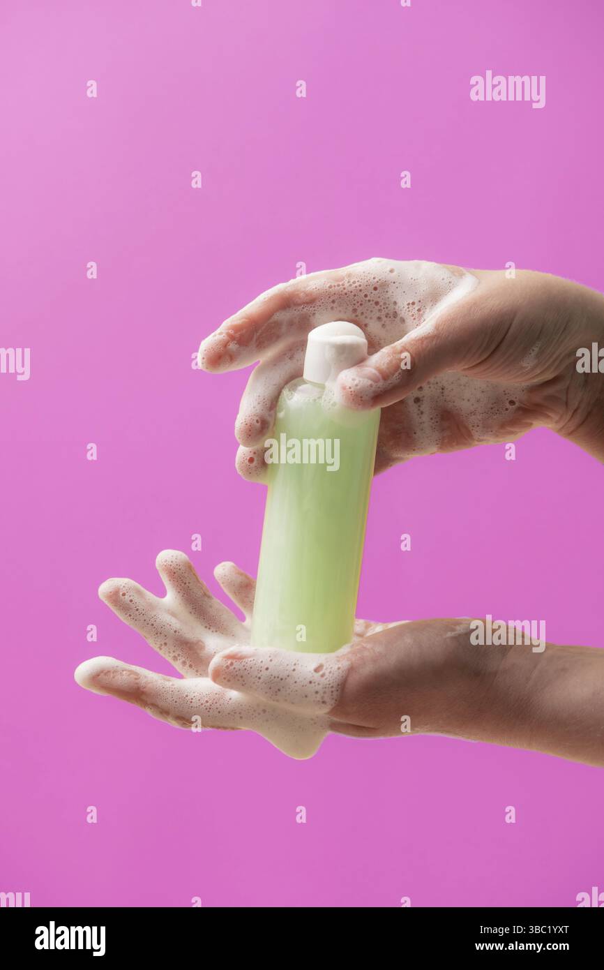 Natürliches Shampoo in der Flasche an den weiblichen Händen mit Schaum. Natürliches kosmetisches Konzept auf rosa Hintergrund Stockfoto