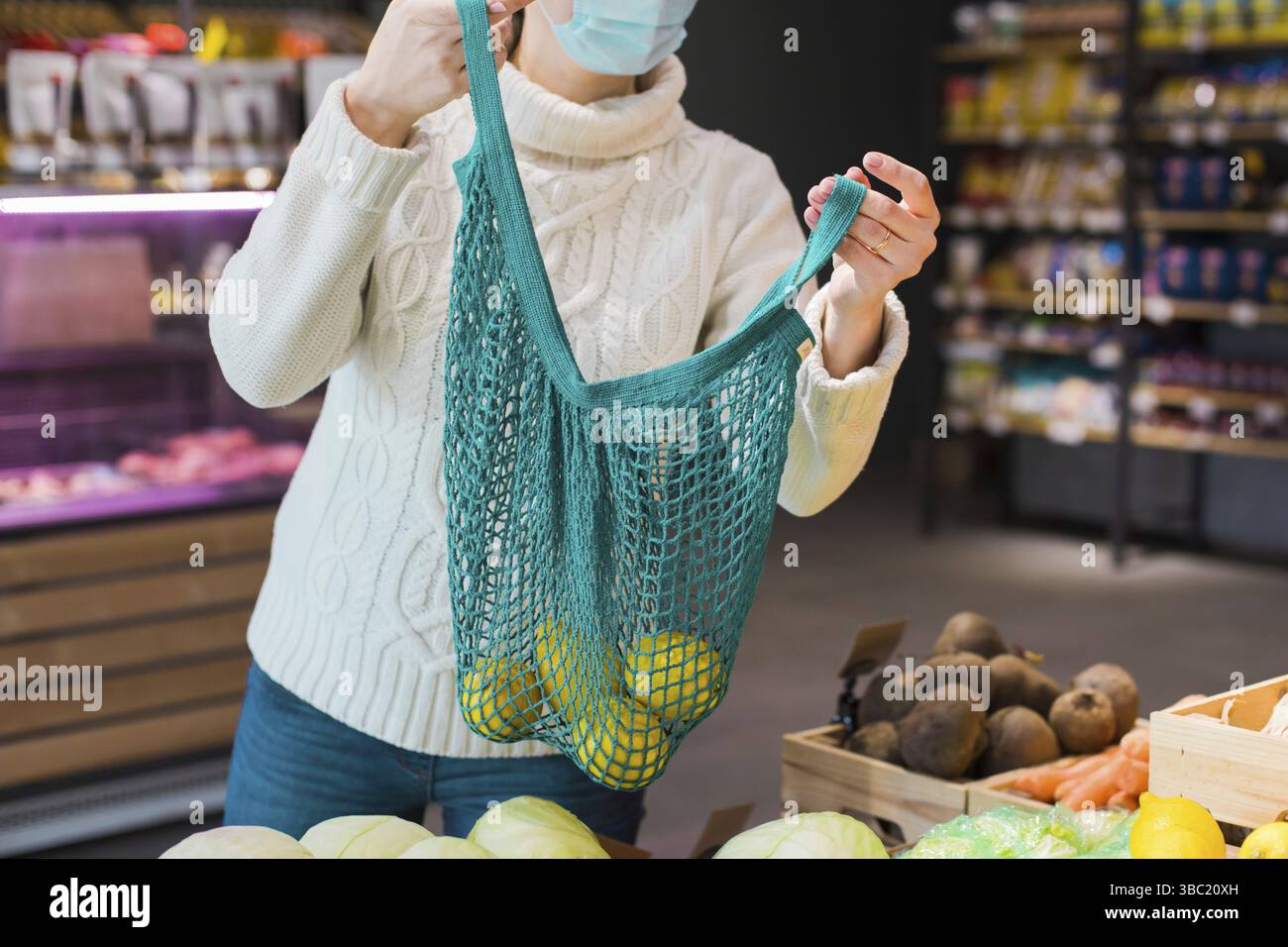 Einkaufen in einem lokalen Bauernhof mit Null-Abfall-Konzept. Frau, die frisches Obst und Gemüse aussucht und in eine blaue Netztasche steckt. Unterstützende Position Stockfoto