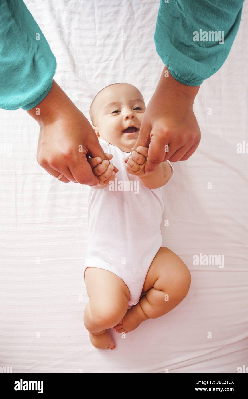 Eine Frau massiert Kinderhände, ein süßes Kind lacht. Draufsicht auf das Bett Stockfoto