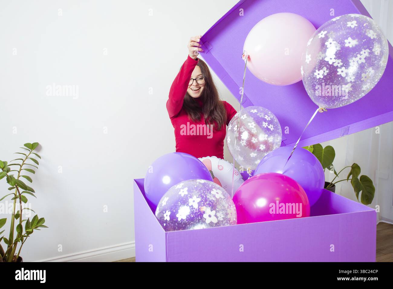 Die glückliche junge Frau öffnet eine große geschenkbox. Die wunderschönen Ballons fliegen aus der Box Stockfoto