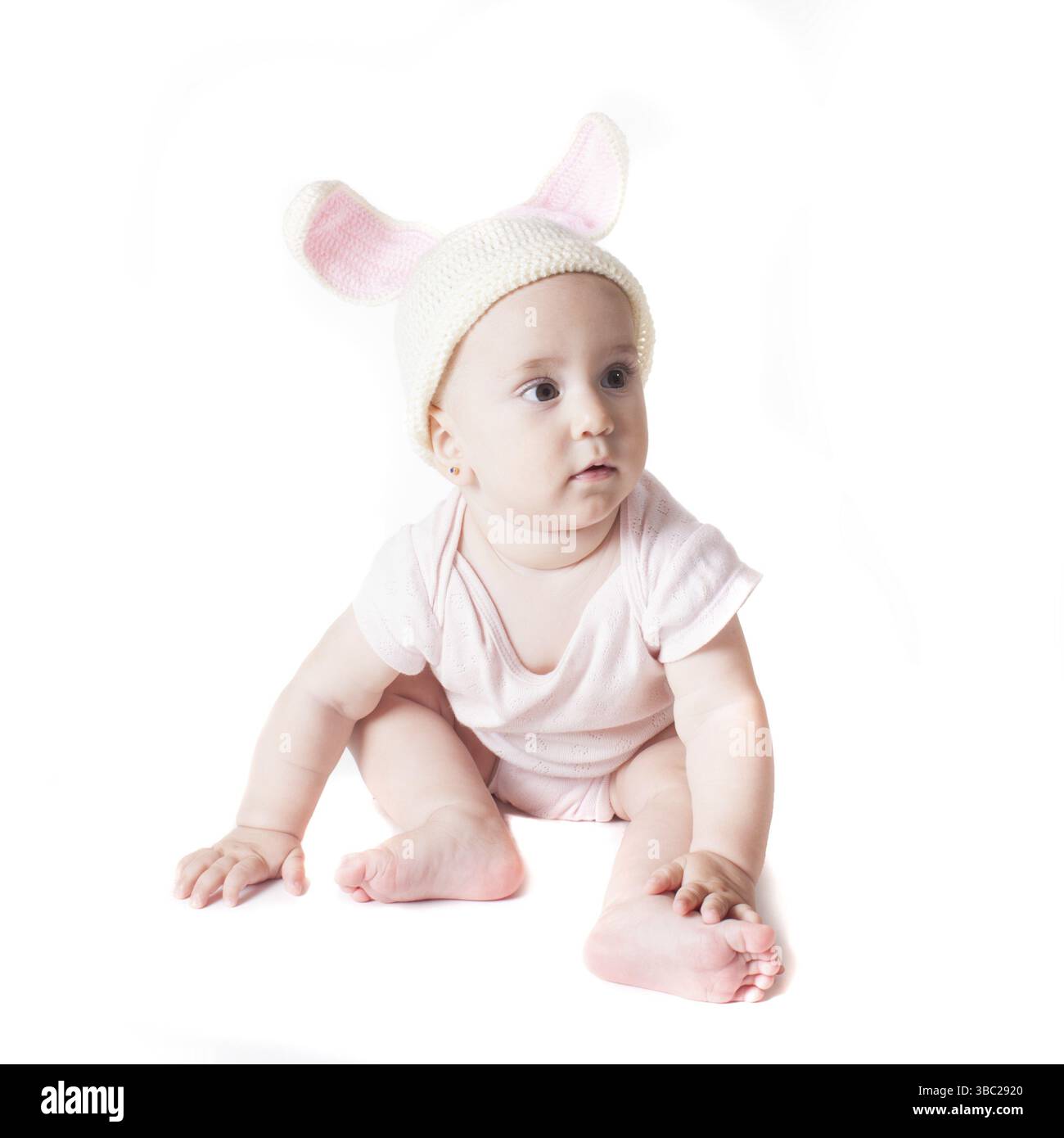 Süßes kleines Mädchen, das in einem gestrickten Hasenmütze sitzt, isoliert auf Weiß Stockfoto