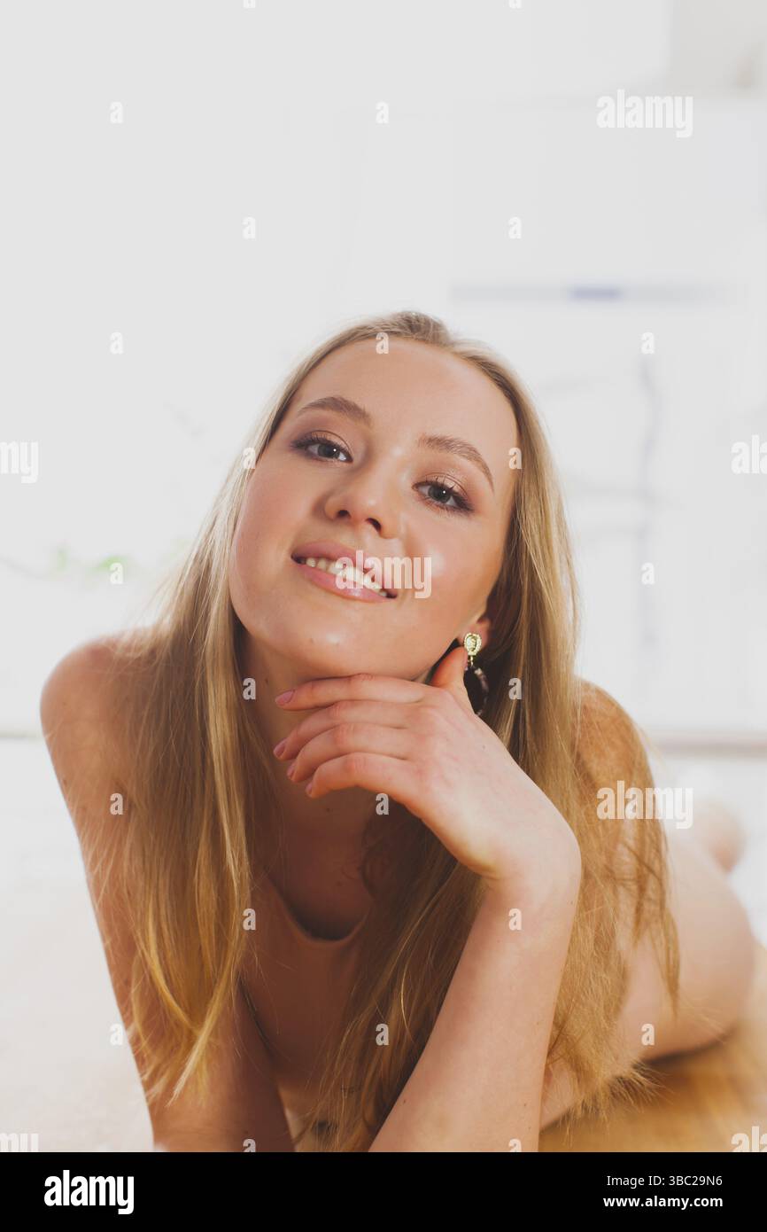 Porträt einer charmanten blonden Frau mit lockerem Haar, die sich auf einem Holzboden posiert. Ein lächelndes Modell, das natürliche Schönheit mit minimalem Make-up zeigt. Whit Stockfoto