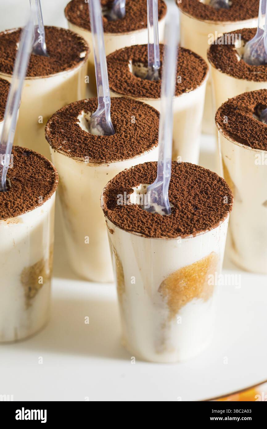 Die Vertiefung von Tiramisu in Plastikbechern mit Plastiklöffeln. Köstliches italienisches Dessert auf einem weißen Stand Stockfoto