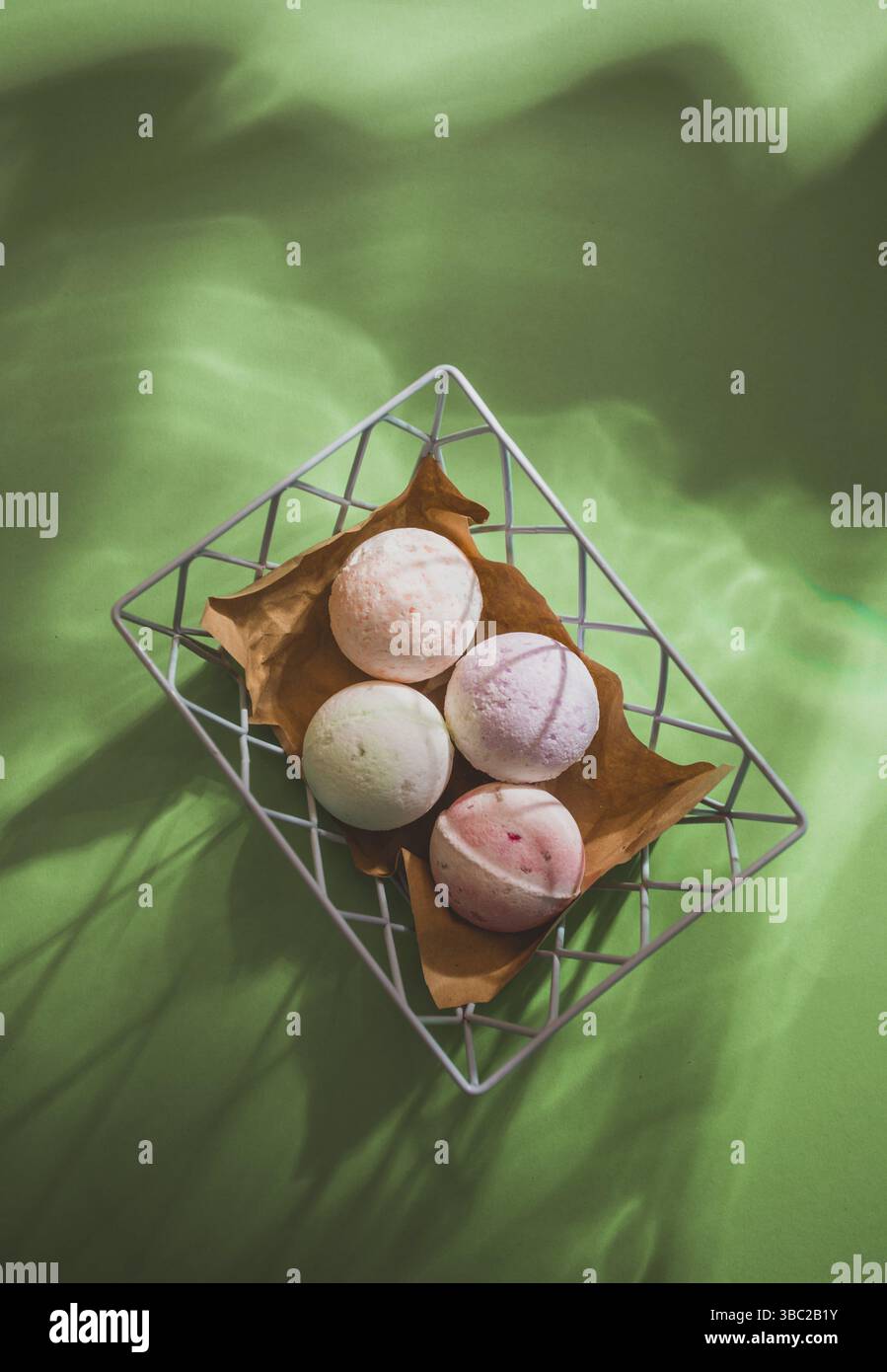 Weiße und rosafarbene Badebomben in einem Korb auf grünem Hintergrund mit beweglichen Wasserschatten. Bio-Kosmetik auf Wellness-Hintergrund Stockfoto