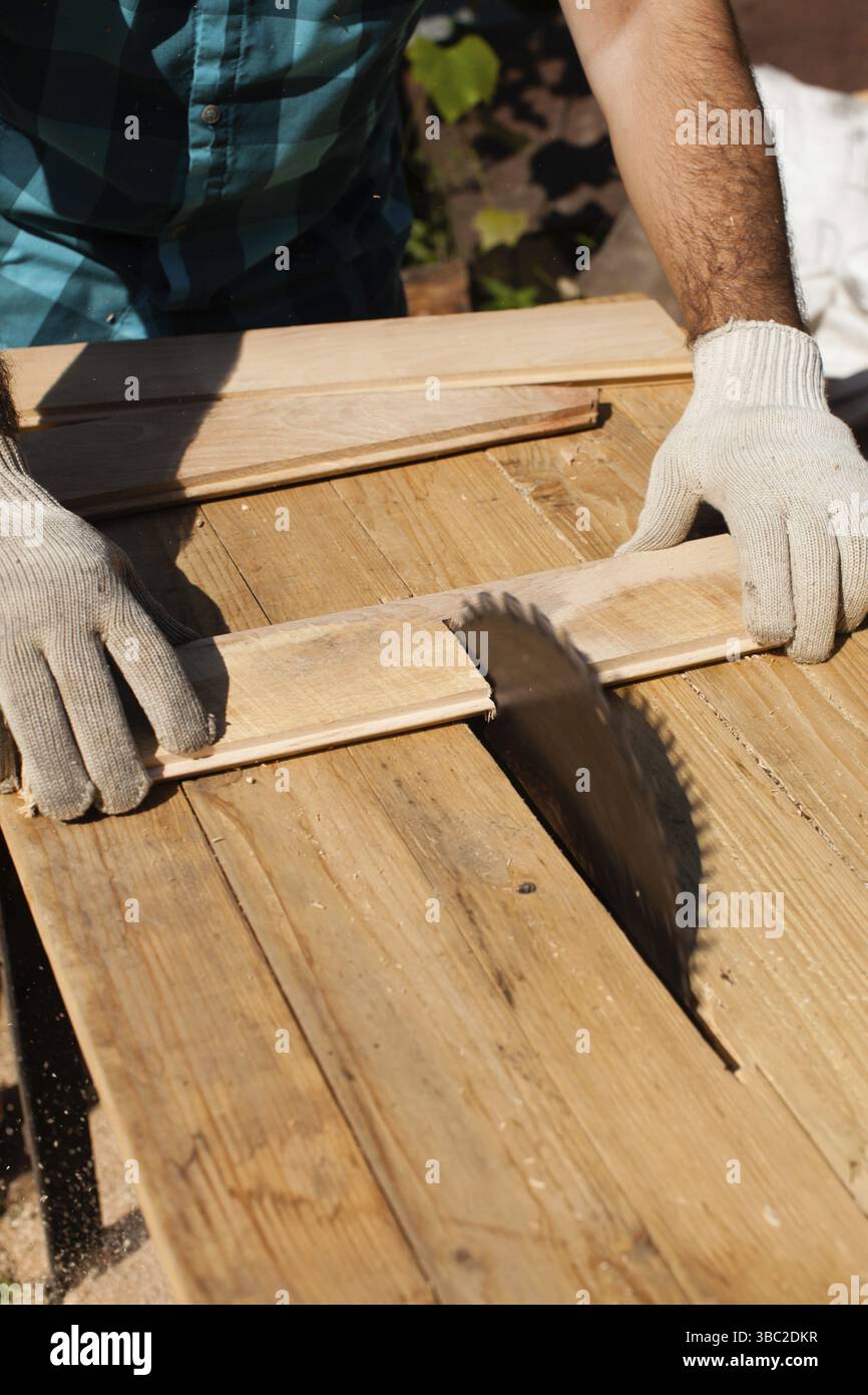 Hart arbeitender Holzarbeiter, der Holzbohlen schneidet, Fokus auf Säge Stockfoto