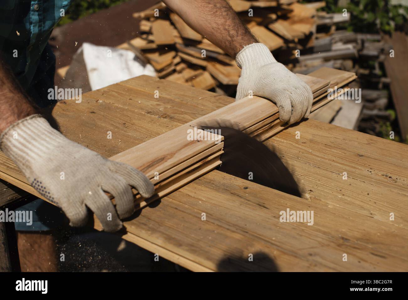 Hart arbeitender Holzarbeiter, der Holzbohlen schneidet, Fokus auf Säge Stockfoto