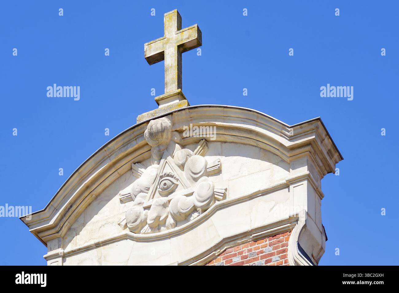 Durch die Kombination religiöser und Freimaurersymbole erhebt sich ein Steinkreuz über dem Auge der Vorsehung auf einem Gebäude und ruft Mysterien und Geschichte hervor Stockfoto
