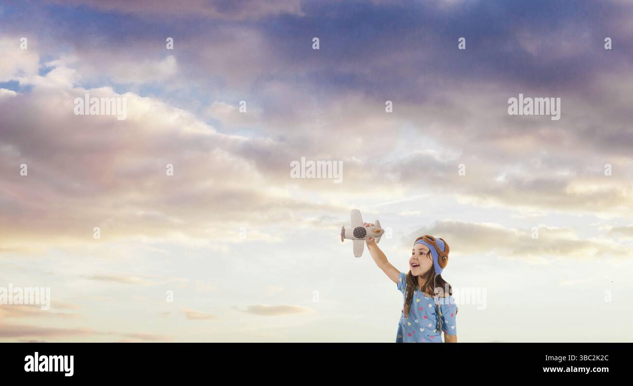 Lächelndes Mädchen mit einem Spielzeugflugzeug in den Armen, träumt davon, Pilot zu werden. Sonnenuntergang am Himmel. Konzept der zukünftigen Generation Stockfoto
