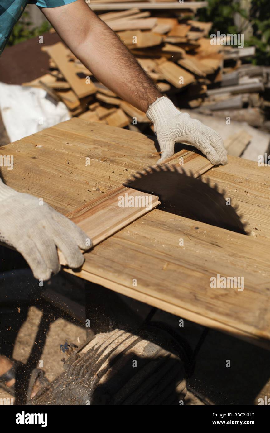 Hart arbeitender Holzarbeiter, der Holzbohlen schneidet, Fokus auf Säge Stockfoto