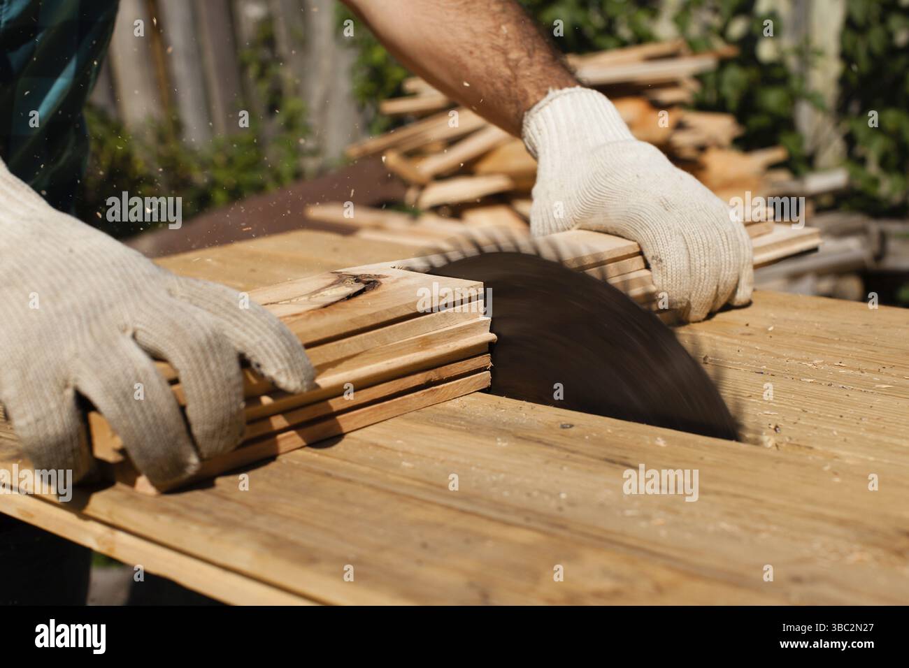 Hart arbeitender Holzarbeiter, der Holzbohlen schneidet, Fokus auf Säge Stockfoto