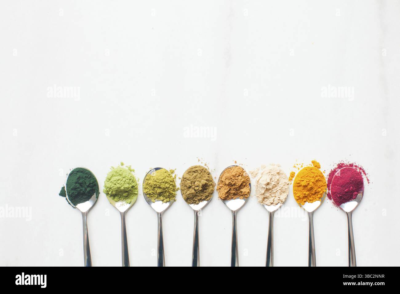 Löffel mit verschiedenen bunten Superfood-Pulvern mit einem kräftigenden Effekt auf dem weißen Marmortisch, Platz für Text Stockfoto