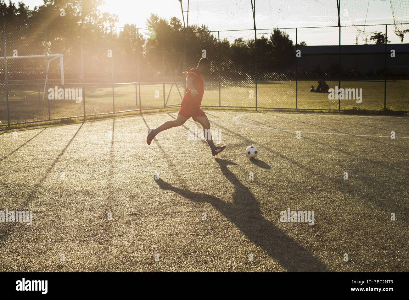 Fußballspieler in Rot. Ein Mann, der draußen im Gras Ball tritt Stockfoto