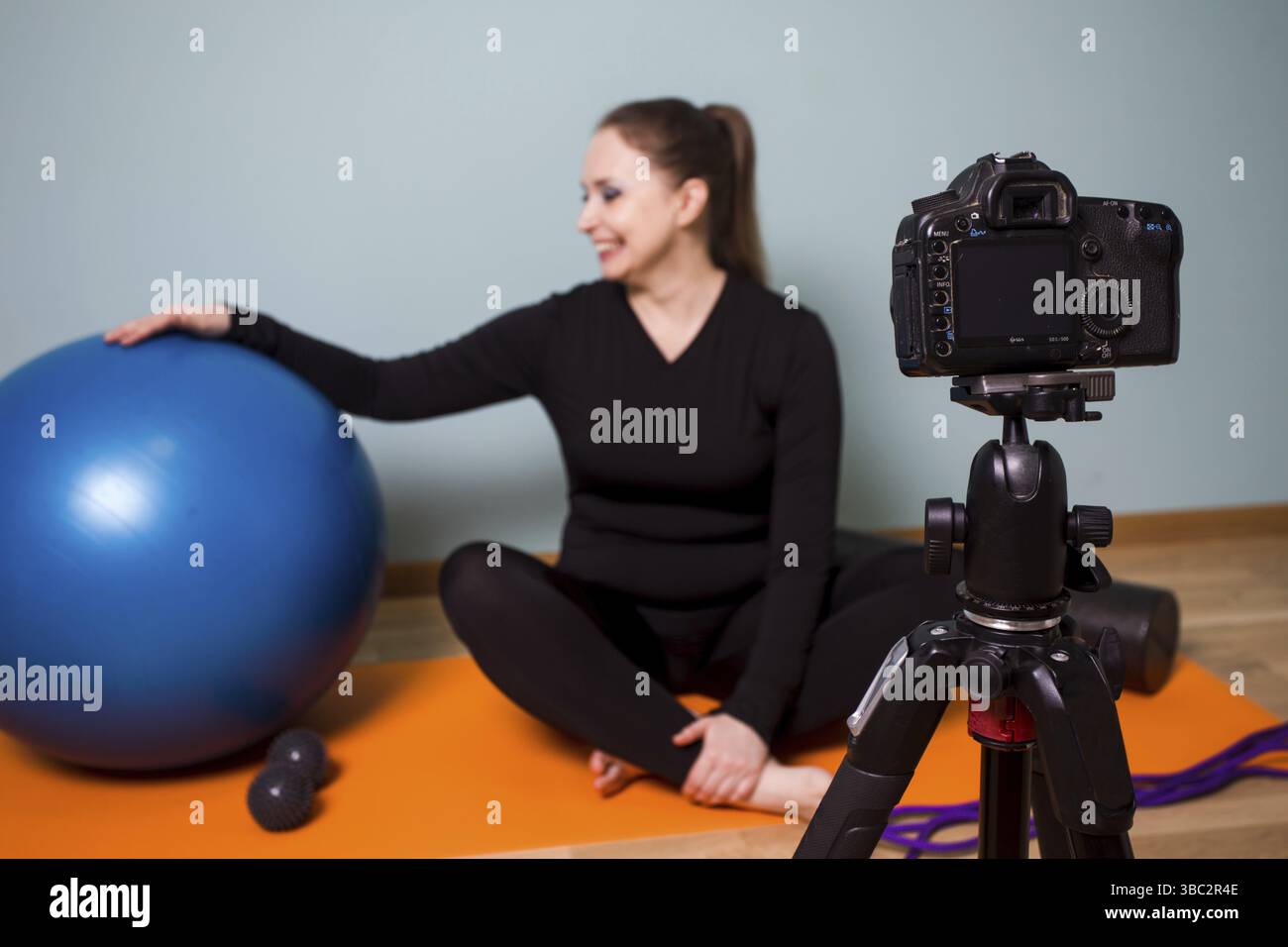 Junge Frau Fitness-Coach in schwarzer Sportbekleidung, macht Video darüber, wie man zu Hause trainiert, während Quarantäne. Vlogging über Workouts und myofasziale r Stockfoto