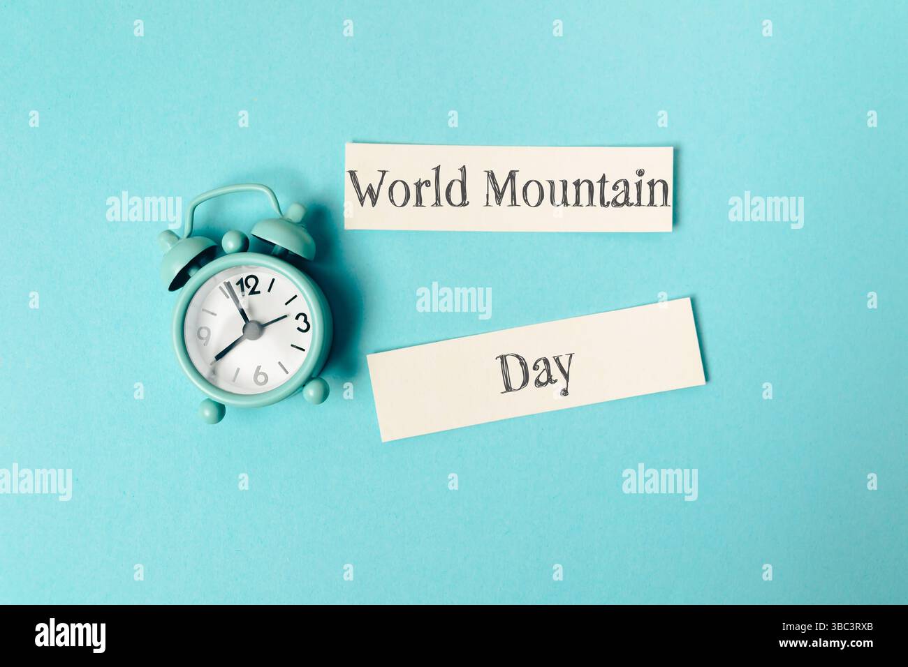 Uhr mit den Händen auf die Zahlen 3 und 9. Ein Stück Papier mit dem Wort World Mountain drauf Stockfoto