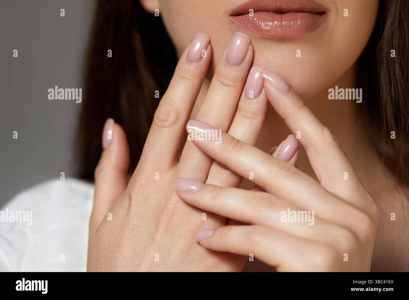 Eine Frau berührt sanft ihre Lippen, während sie ihre gepflegten Hände mit einer gepflegten Maniküre in dezenten Pastelltönen unter warmem Licht zeigt. Stockfoto