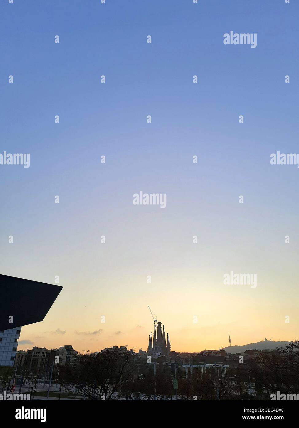 Die Basilika Sagrada Familia steht bei Sonnenuntergang mit goldenen Tönen am Himmel über der Stadtlandschaft Barcelonas Stockfoto