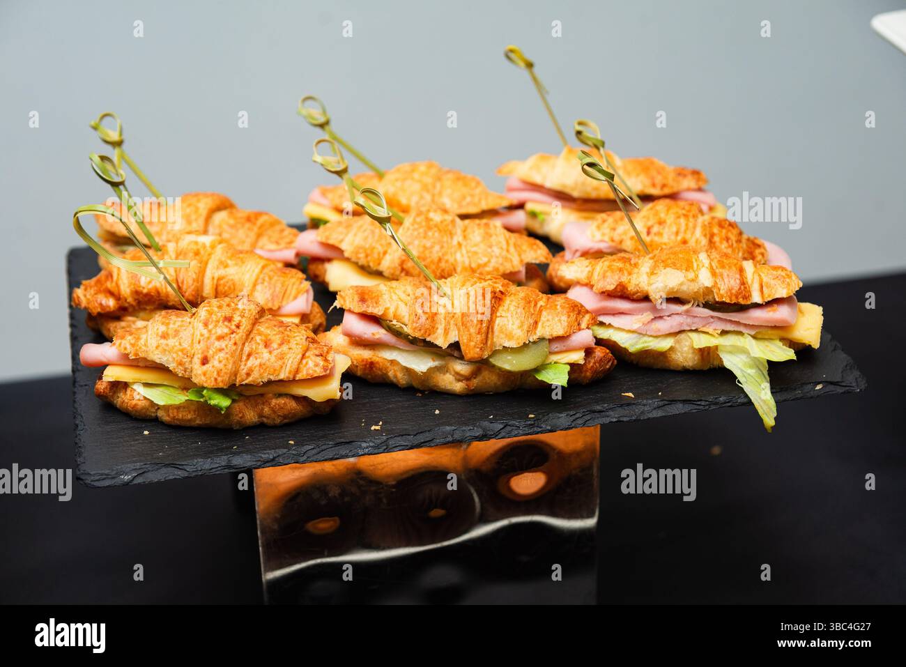Tablett mit Mini-Croissant-Sandwiches gefüllt mit Schinken, Käse und Salat, ordentlich für ein Catering-Event oder Brunch angeordnet. Stockfoto
