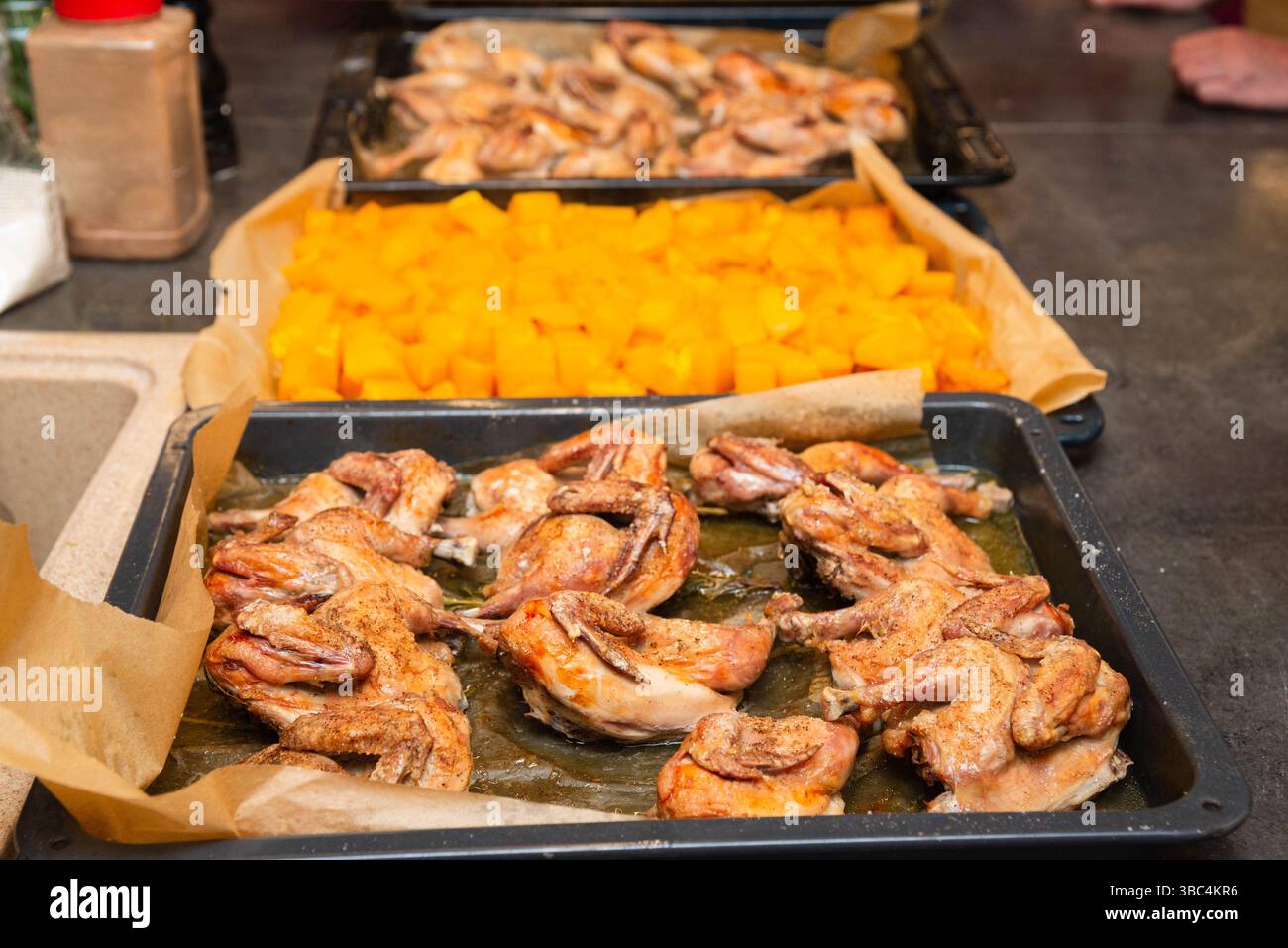 Mehrere Tabletts gebratene Wachteln und gewürzter Butternusskürbis, frisch aus dem Ofen und bereit für ein Gourmetgericht oder Buffet. Stockfoto
