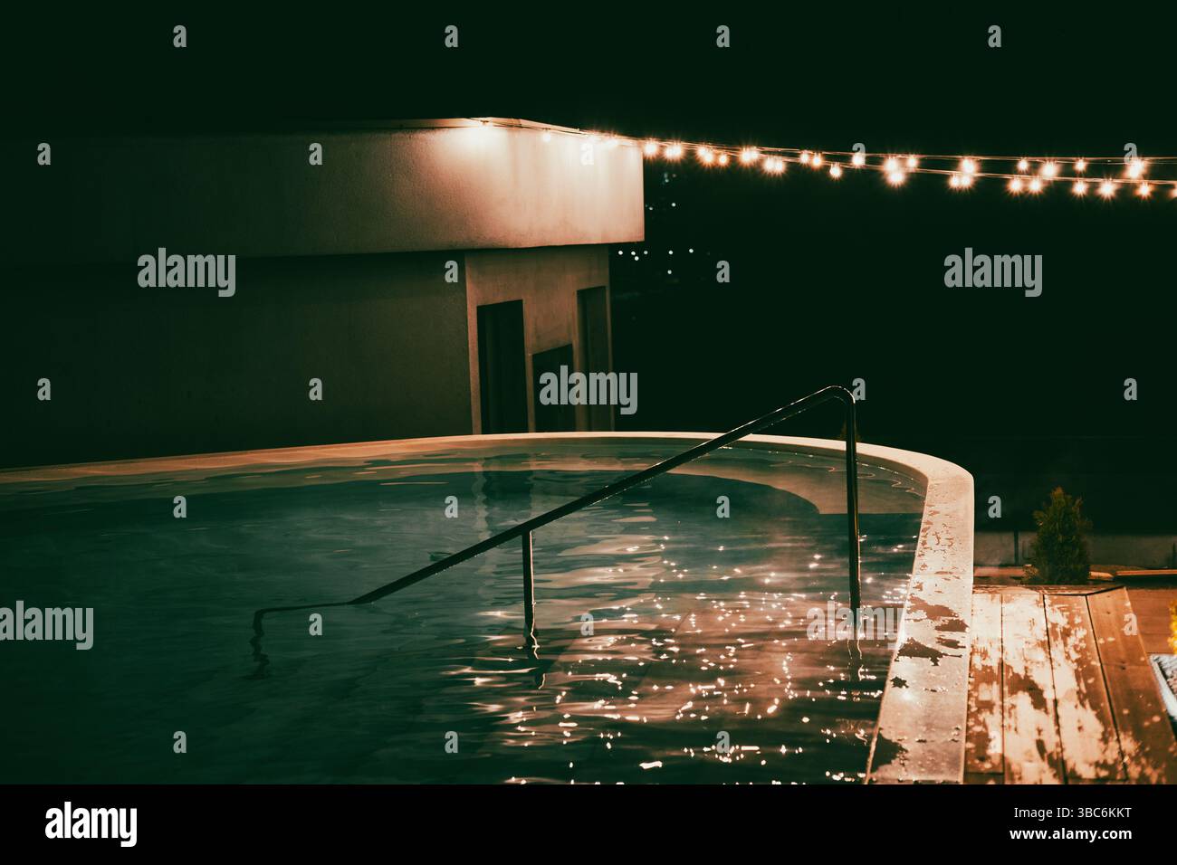 Eine faszinierende Nachtszene zeigt einen Pool mit glitzerndem Wasser unter einer Girlande. Ein Pool, der von sanften Lichtern und einer Reihe dekorativer Glühbirnen beleuchtet wird. Stockfoto