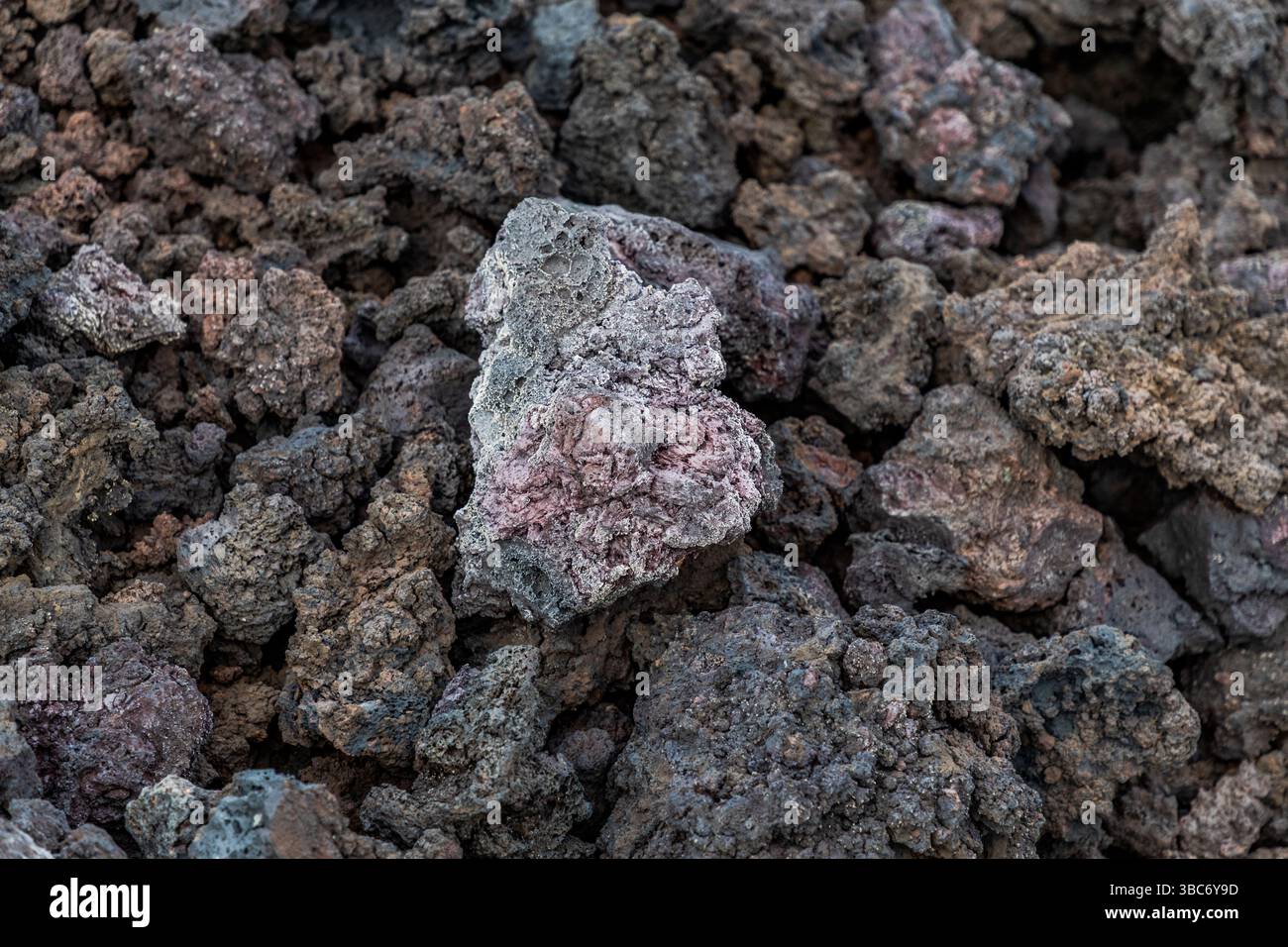 Poröses Vulkangestein liegt zwischen dunklen Lavablöcken entlang der Avenida Marítima in der Nähe von El Golfo auf Lanzarote, Kanarische Inseln, Spanien. Ein hellgrauer Stein mit rötlichen Einschlüssen hebt sich von dem schwarzbraunen Lavafeld ab. Stockfoto