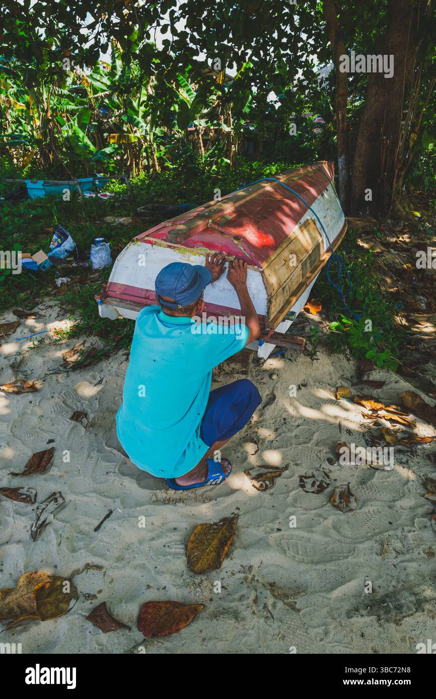 Balikpapan, Indonesien - 20. April 2025. Der alte Mann hockt und flickt sein Boot morgens in der Nähe des Strandes. Stockfoto