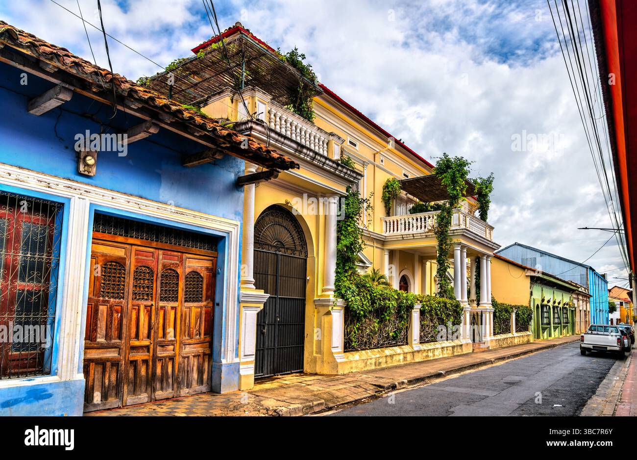 Eine Reihe von lebhaften Häusern im Kolonialstil mit kunstvollen Balkonen, Bogenfenstern und üppigem Grün säumt eine enge Kopfsteinpflasterstraße in Granada, Nicaragua. Die Pastellfarben und architektonischen Details spiegeln den Charme und die Geschichte des gut erhaltenen kolonialen Erbes der Stadt wider Stockfoto