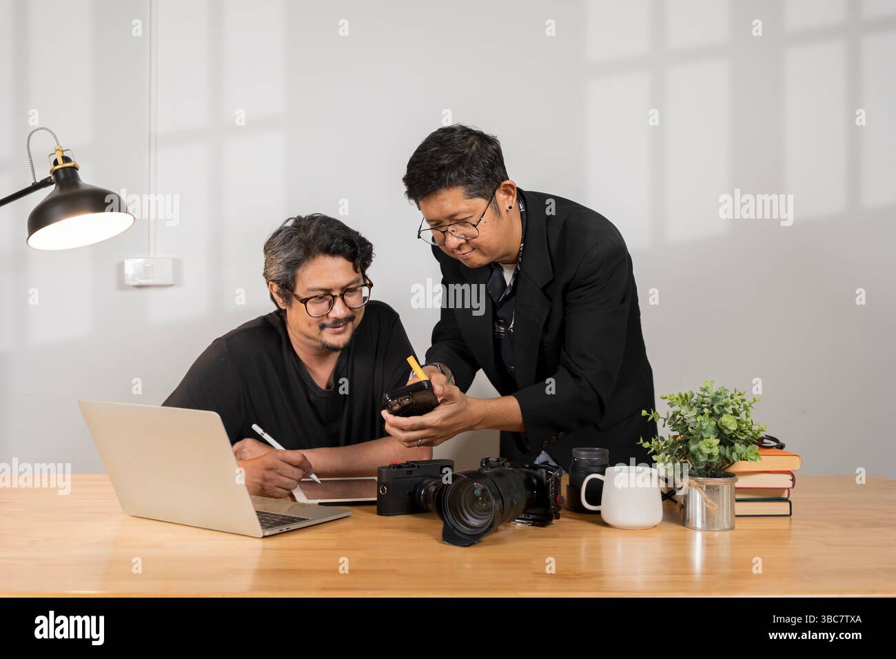 Professioneller Fotograf, der mit der Kamera unterrichtet, während er die Fotoeinrichtung im Studio bespricht. Kreative Teamarbeit, Schulungen, digitaler Workflow, Mento Stockfoto