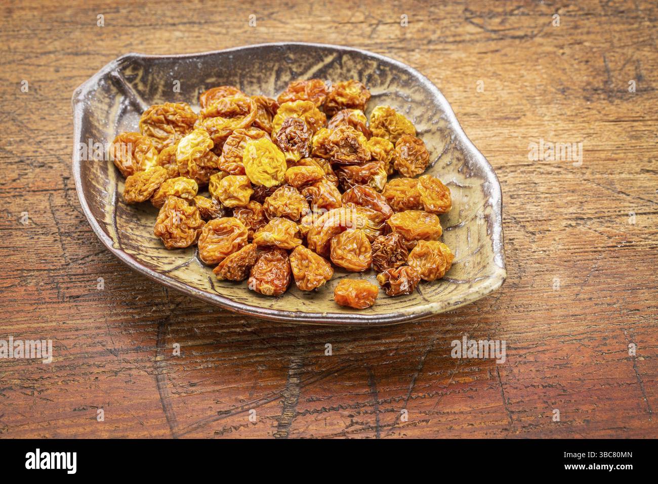Getrocknete Goldbeeren in einer blattförmigen Keramikschale gegen rustikales Kratzholz Stockfoto