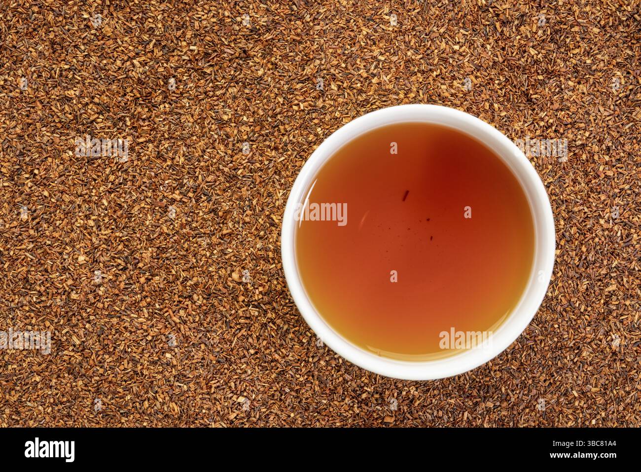 Rooibos Red Tea – eine weiße Tasse heißes Getränk vor dem Hintergrund lockerer Blätter, Tee aus dem südafrikanischen roten Busch, natürlich koffeinfrei Stockfoto